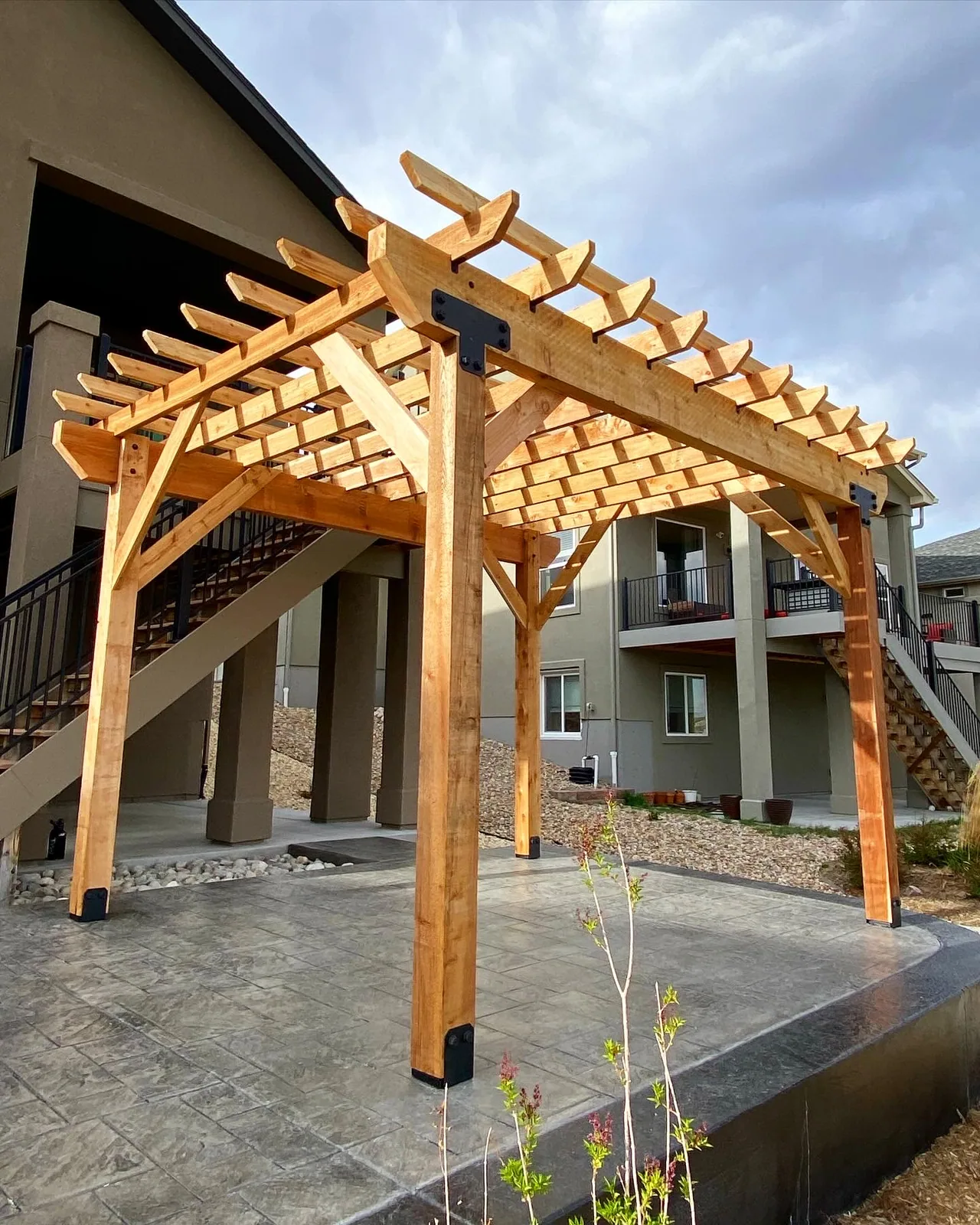 A detached cedar pergola on a patio beside an exterior stair